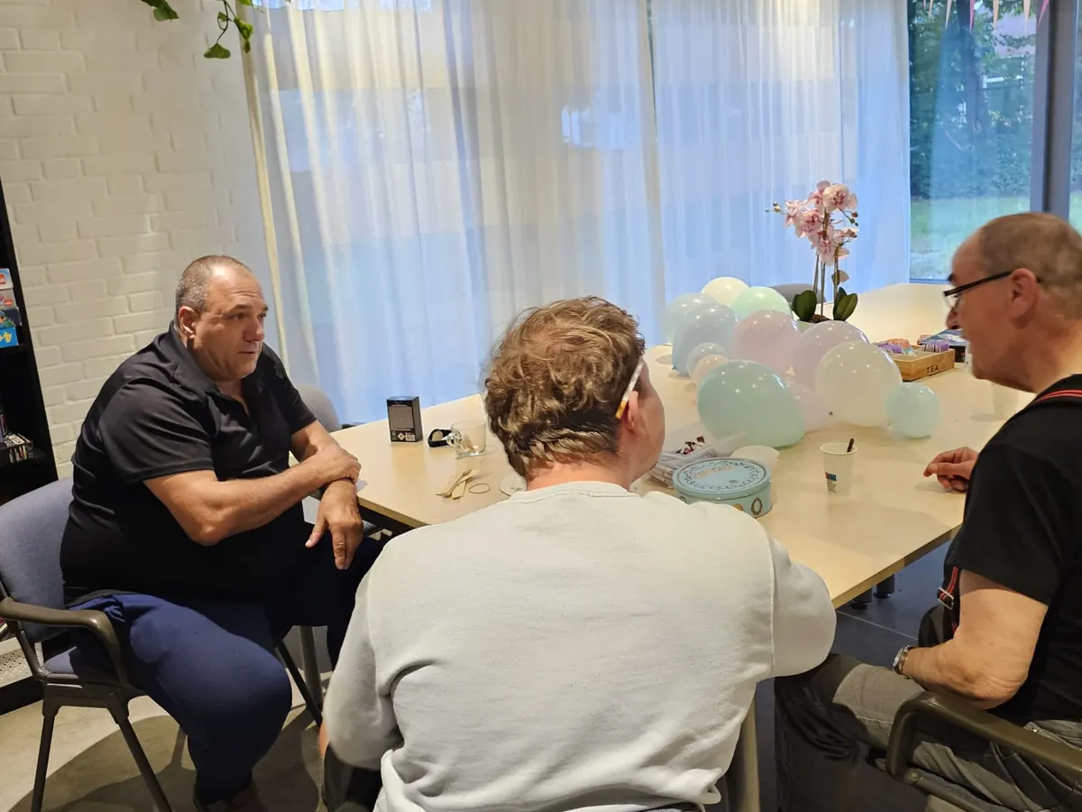 Drie mensen in gesprek aan de lange tafel, met ballonnen en een orchidee tussen hen in.