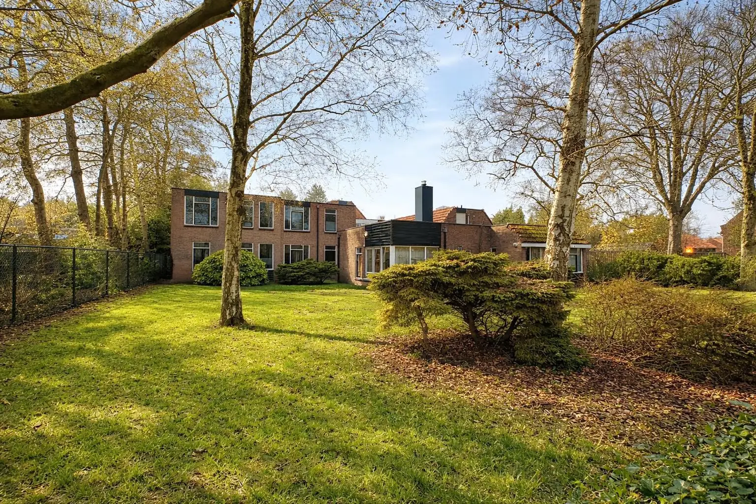 Het pand van Dream Team Noord in Sappemeer, gezien vanuit de tuin, met gras en oude bomen op de voorgrond.