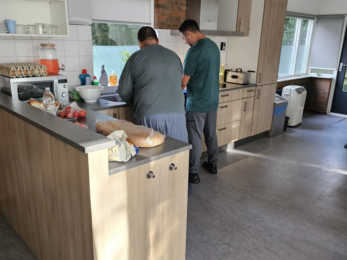 Twee mannen koken samen in de keuken van het huis, met hun rug naar de camera.