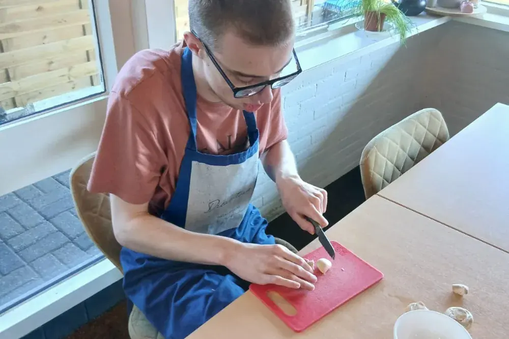 Iemand snijdt aan tafel op een rode snijplank, met een schort voor.