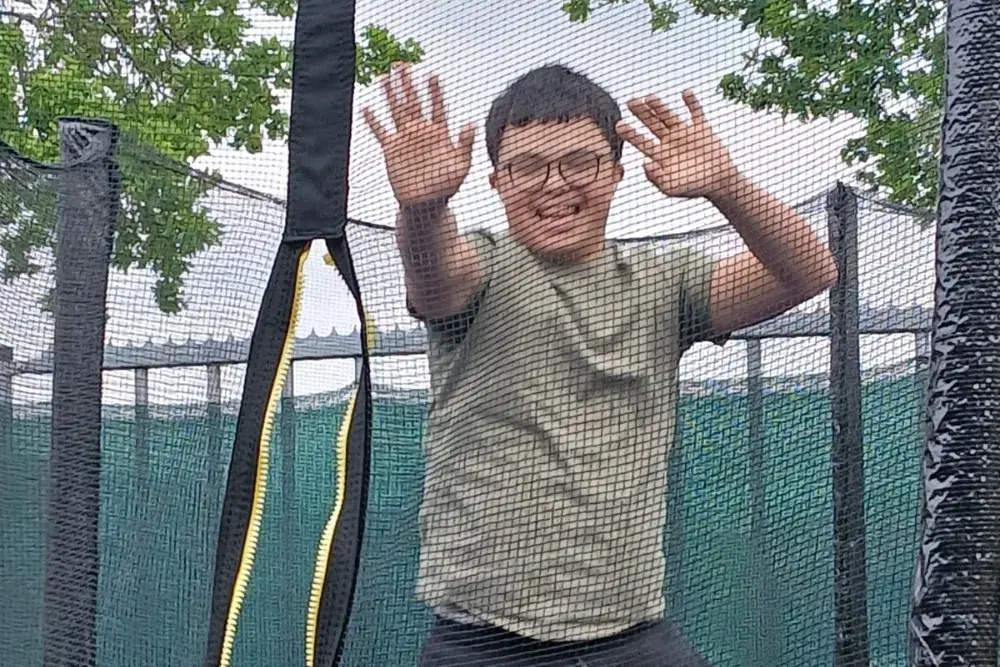 Iemand staat met de armen omhoog op de trampoline in de tuin.